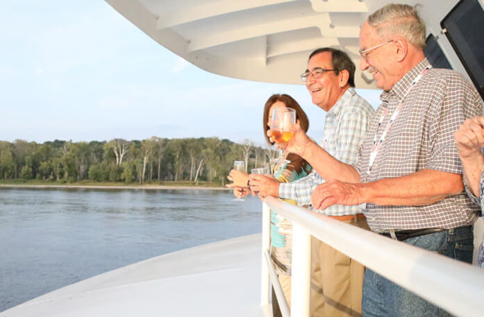 Passengers onboard ship with wine glasses in hand looking out over the river