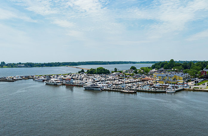 An aerial view of boats docked along Long Island Sound in Old Saybrook. On the shore, there is a large yellow building surrounded by tall, thick trees.