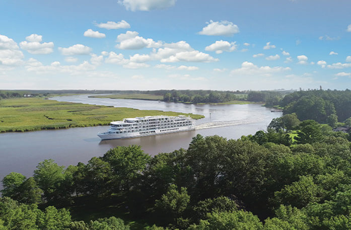 An American riverboat gliding along the Mississippi River, surrounded by green landscapes, under a blue sky with a few clouds.