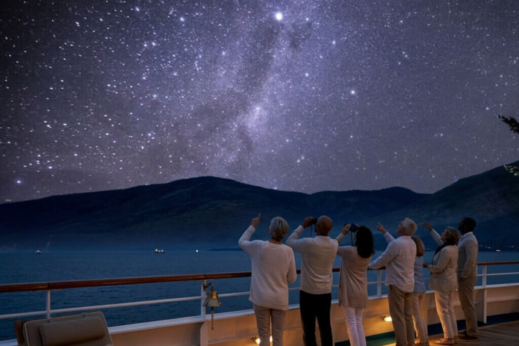 Cruise guests onboard ship at night, gazing into the star-filled sky