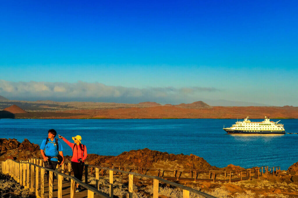 A couple hiking on the Galapagos Islands with a Lindblad ship in the background