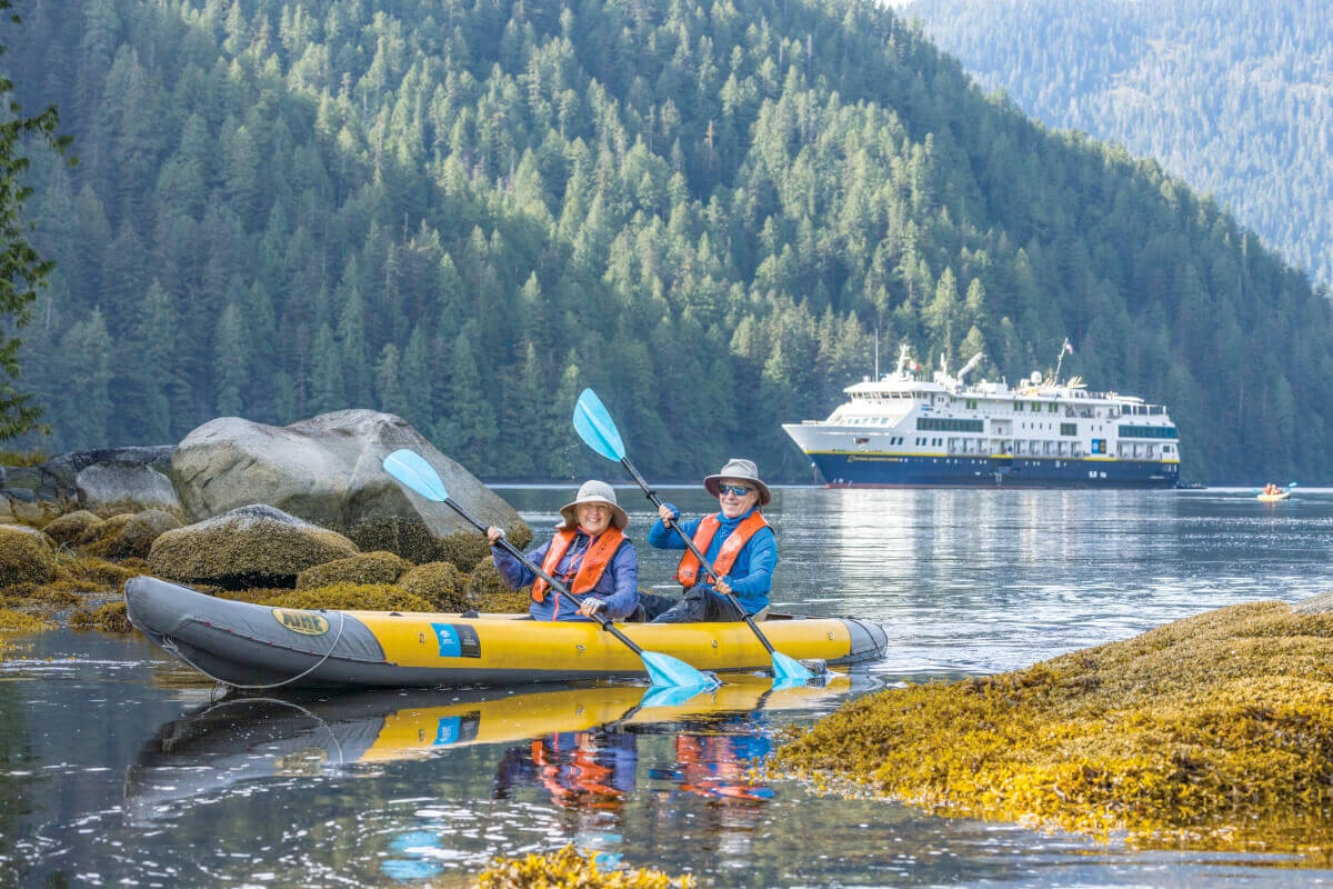A couple of kayakers exploring the coastline with a National Geographic expedition ship in the background