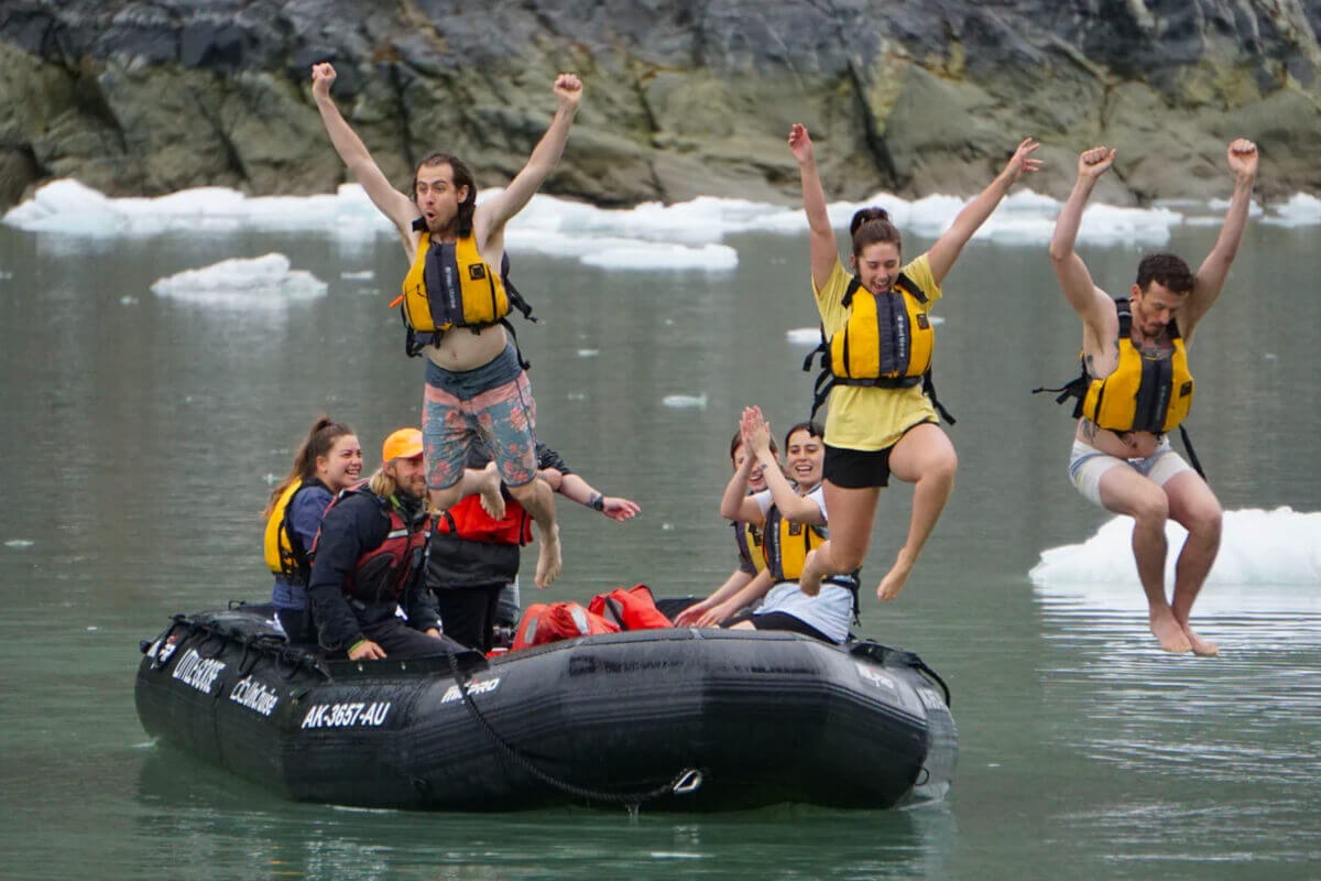 Cruise guests jump from an inflatable skiff into the icy water near a glacier