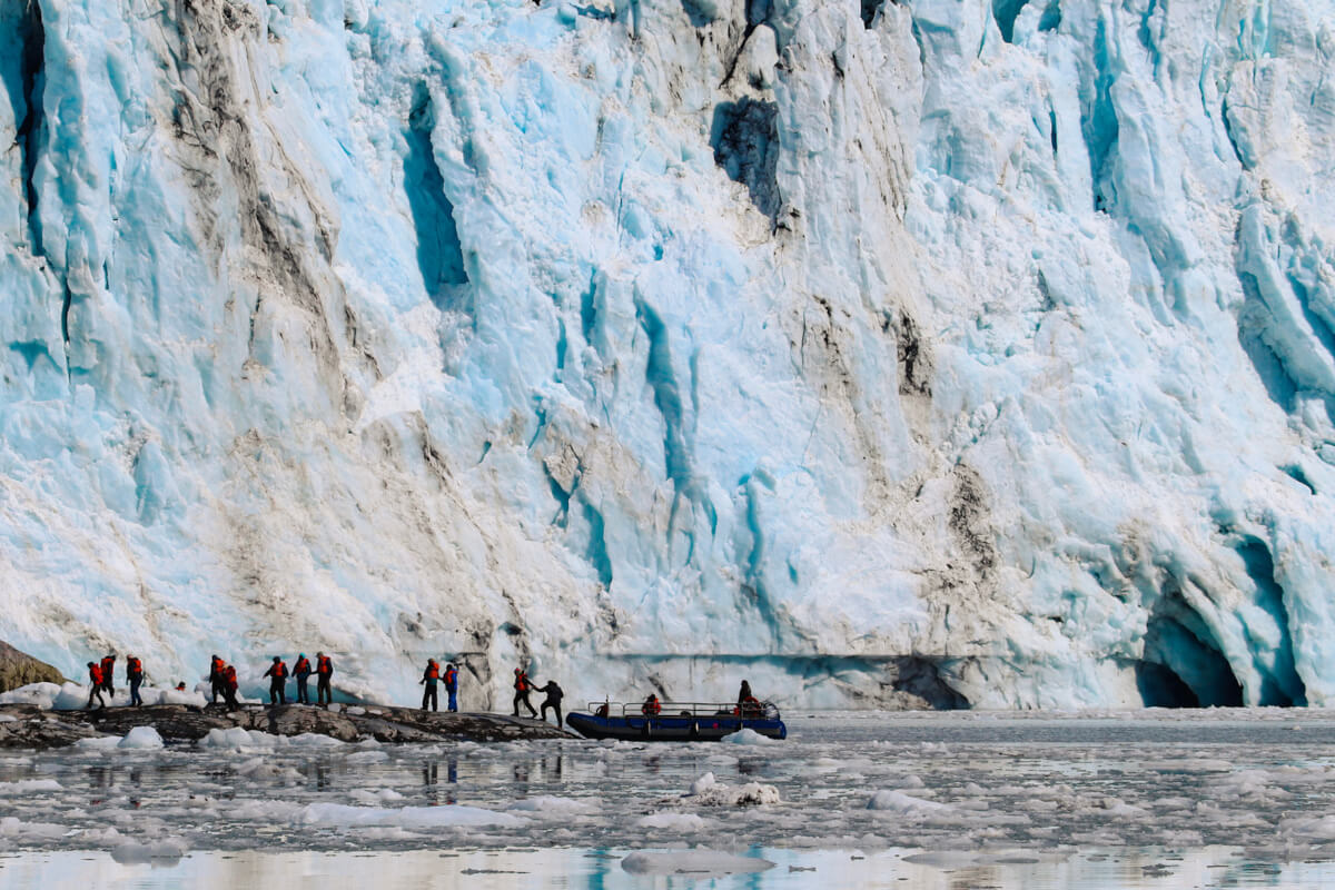 Hikers dwarfed in front of a large glacier