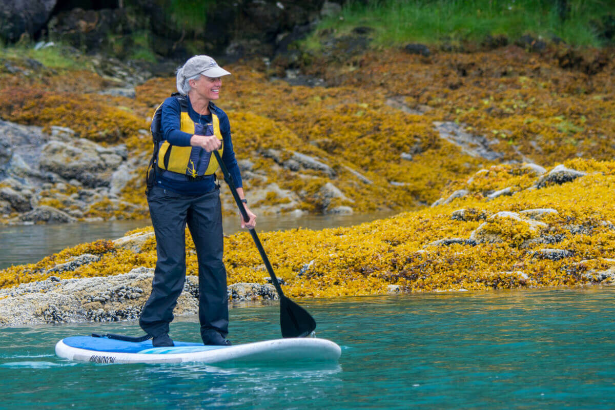 A female cruise guest on a paddleboard exploring Alaska colorful coastline
