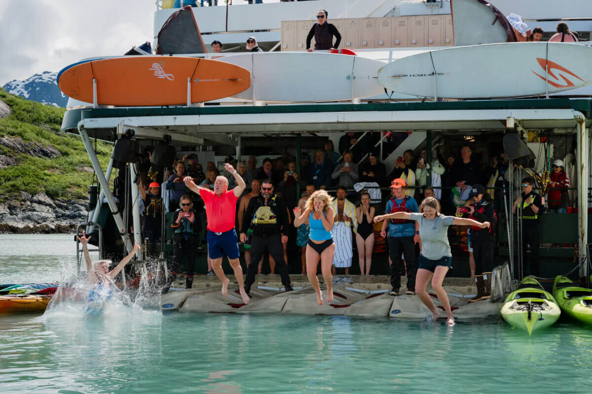Three cruise guests leaping off ship into the glacial cold waters of Alaska