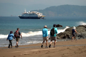 Guests Enjoy a Beach Walk with Safari Voyager in the Distance