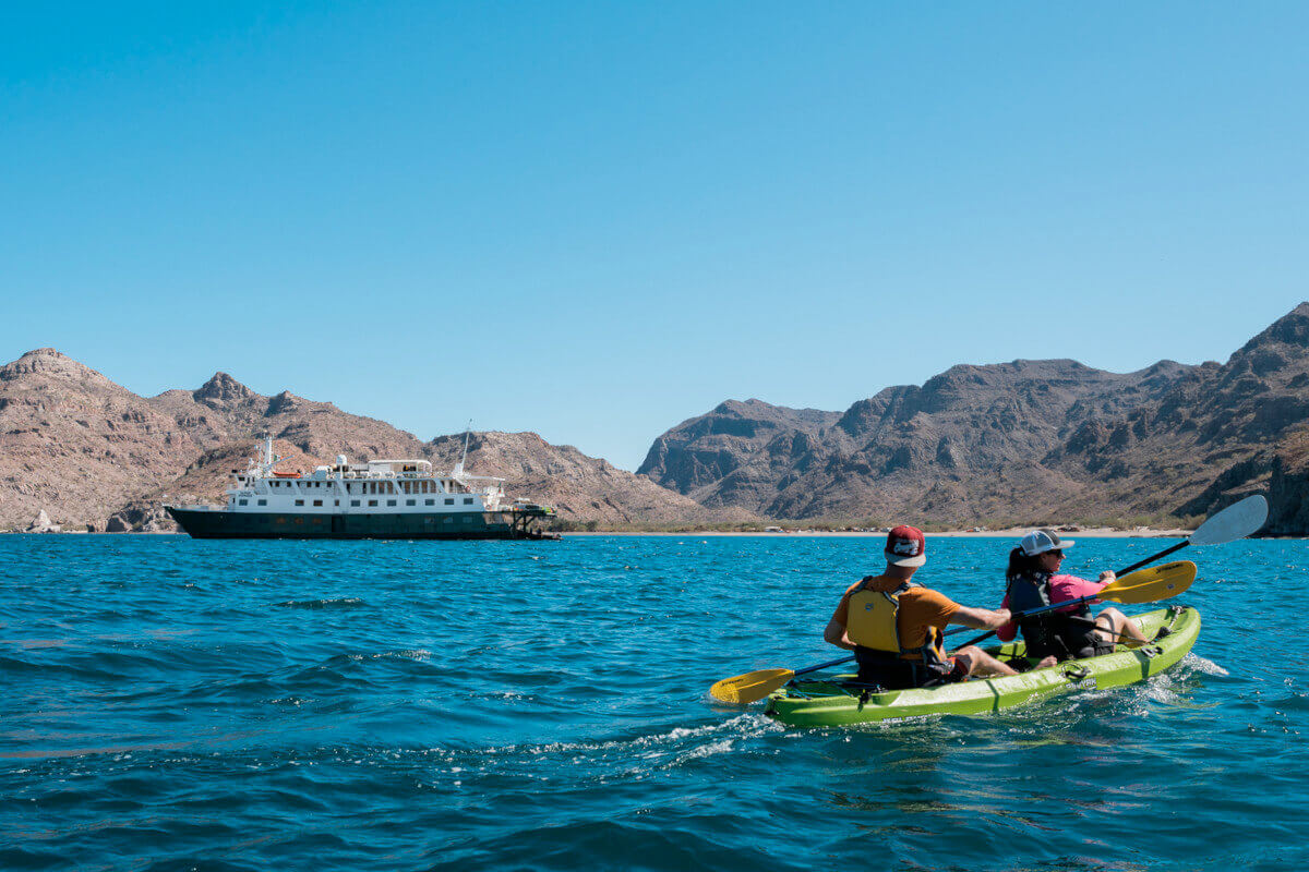 Safari Voyager along the Baja coast, with a pair of kayakers in the foreground