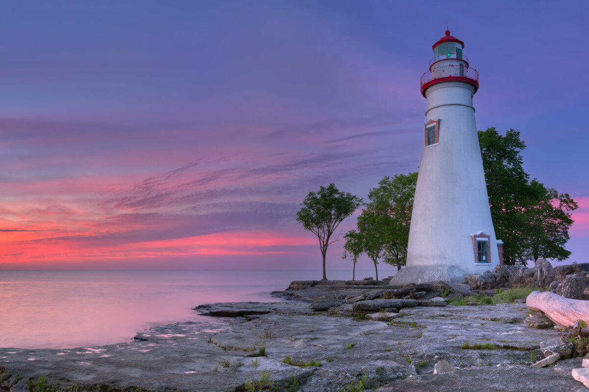 A Great Lakes lighthouse in the foreground with a setting sun over a great lake.