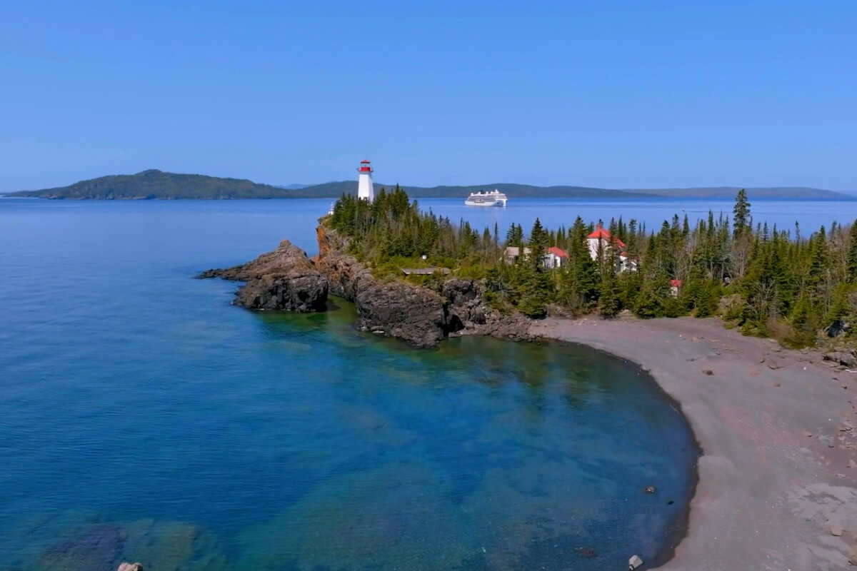 Viking expedition ship sailing on the Great Lakes near a shoreline with a lighthouse