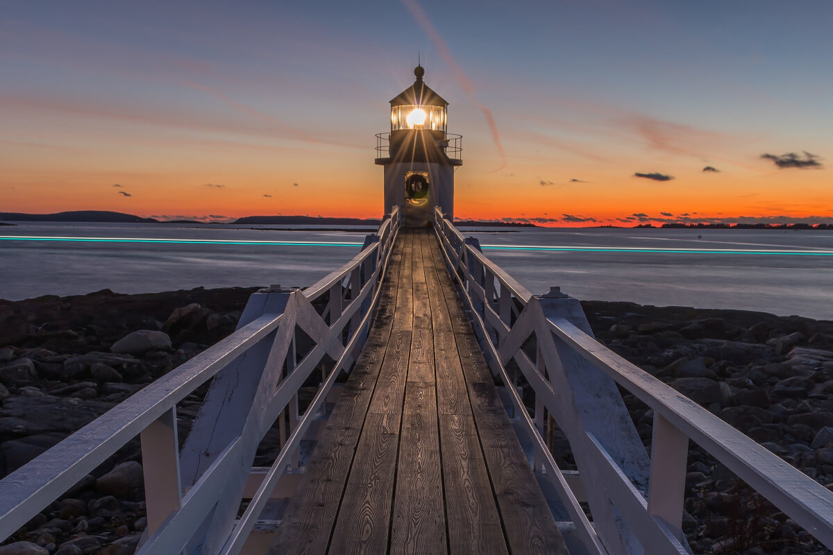 A lighthouse with a walkway leading to it at sunset