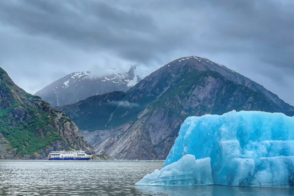 National Geographic ship in the distances, a blue ice berg in the foreground, in Tracy Arm