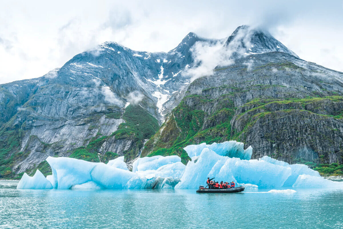 A zodiac filled with cruise passengers exploring up close to an icy blue iceberg in Tracy Arm