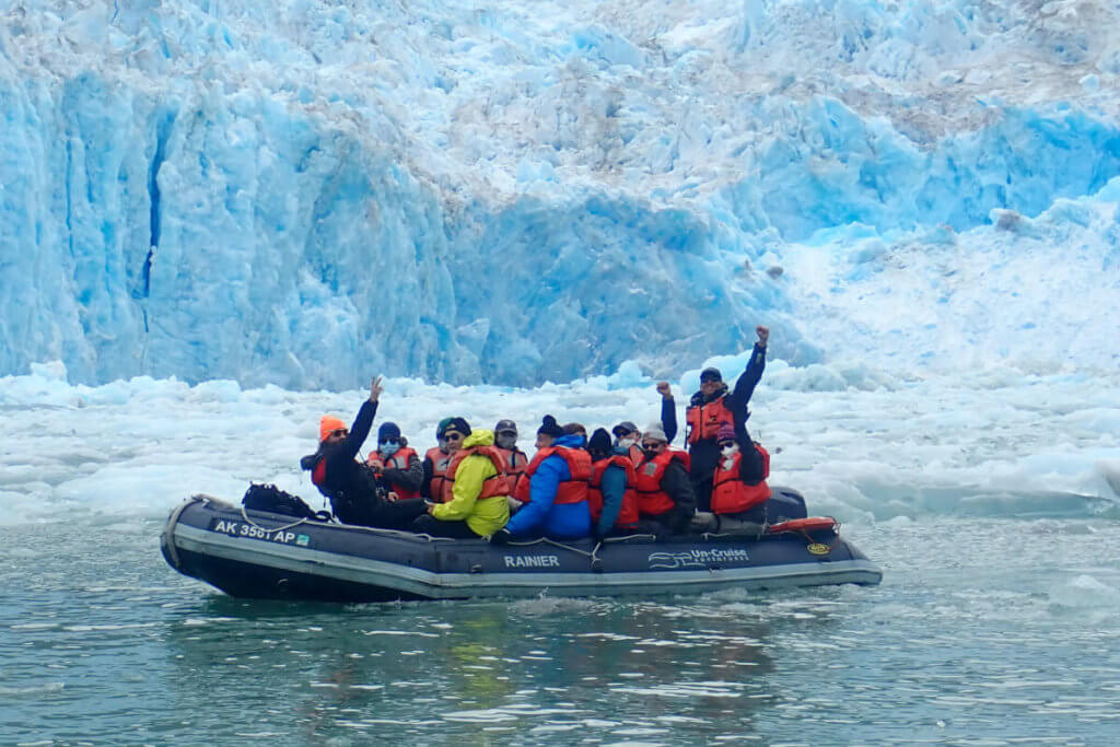 A zodiac filled with guests at the base of a glacier