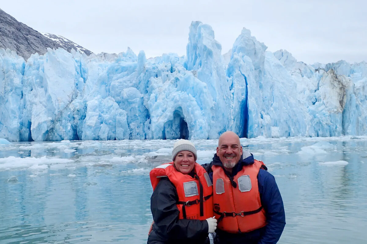 A cruise couple pose in front of a huge glacier